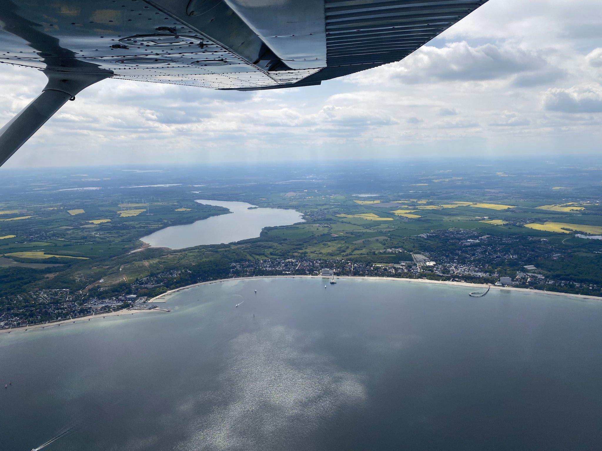 Blick unter einer Tragfläche auf Küste, Meer und Landschaft aus einem Kleinflugzeug