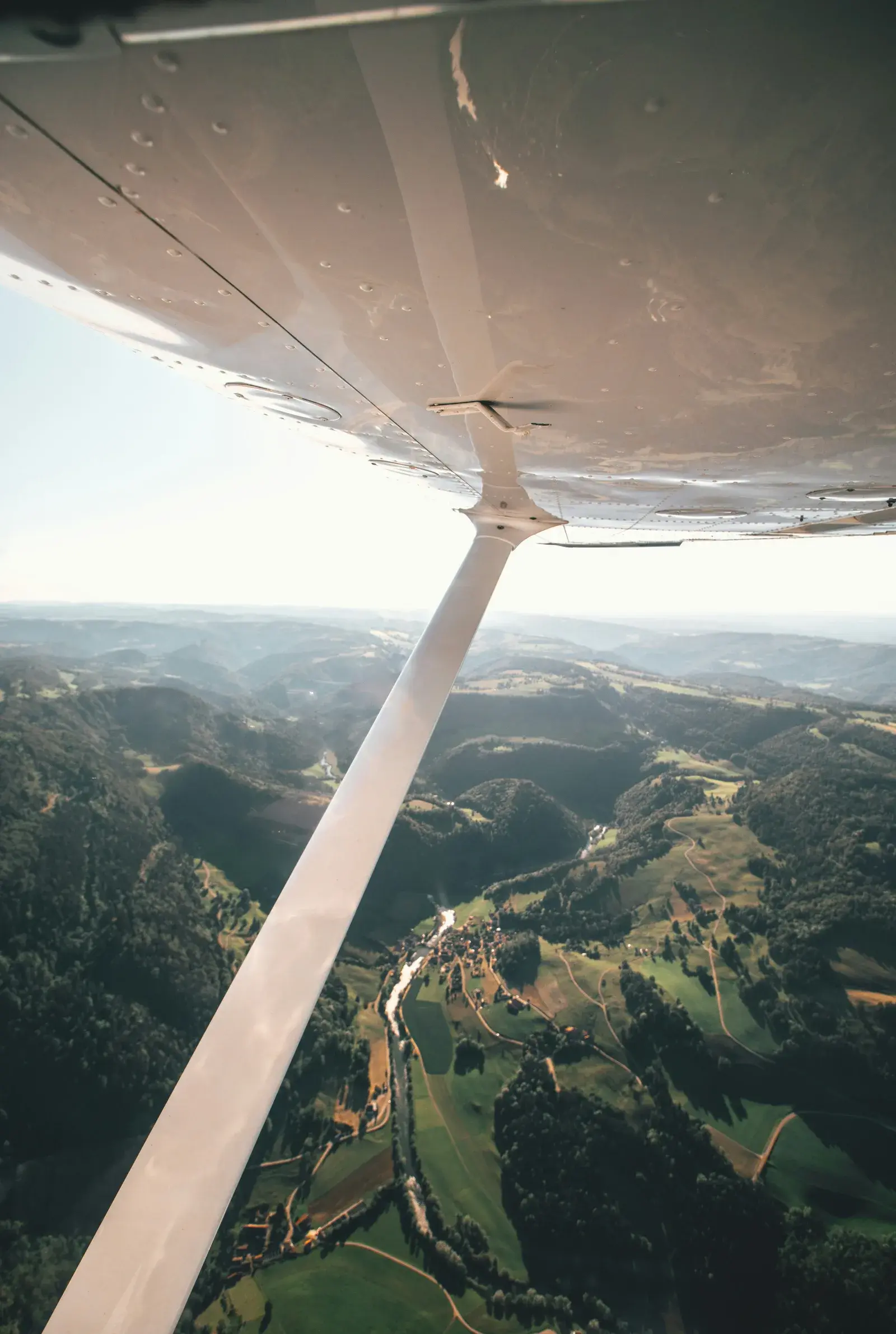 Blick aus einer Cessna unter der Tragfläche hindurch auf ein bewaldetes Tal mit Dörfern